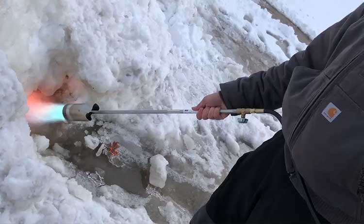 Handheld gas torch melting ice and snow at a swine facility.